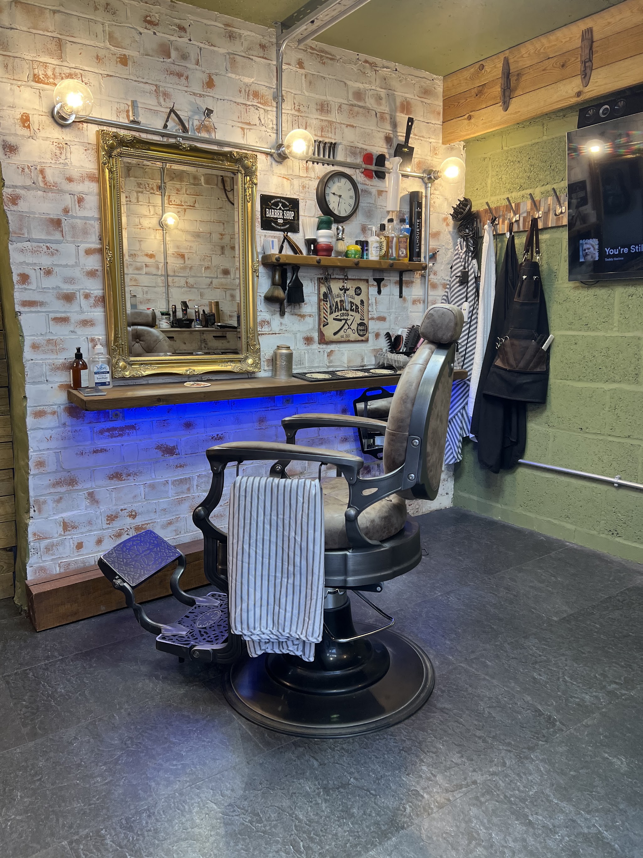The Studio G barber's chair with a striped towel, in front of a gilt mirror and a brick wall