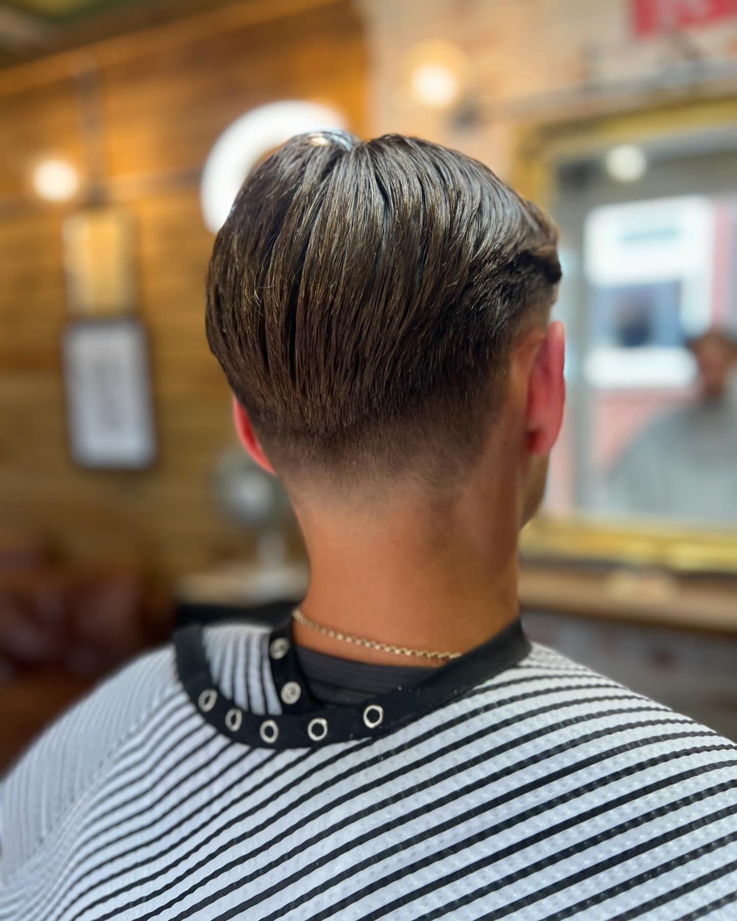 A longer cut with a tapered neckline, from behind, in a striped cape