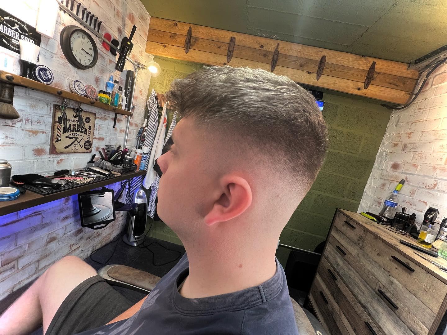 A fresh crop with a fade, in the shop with its brick wall, shelves and blue shelf light